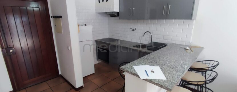 Cozinha com fogão, forno, exaustor, frigorífico e bancada com 3 bancos